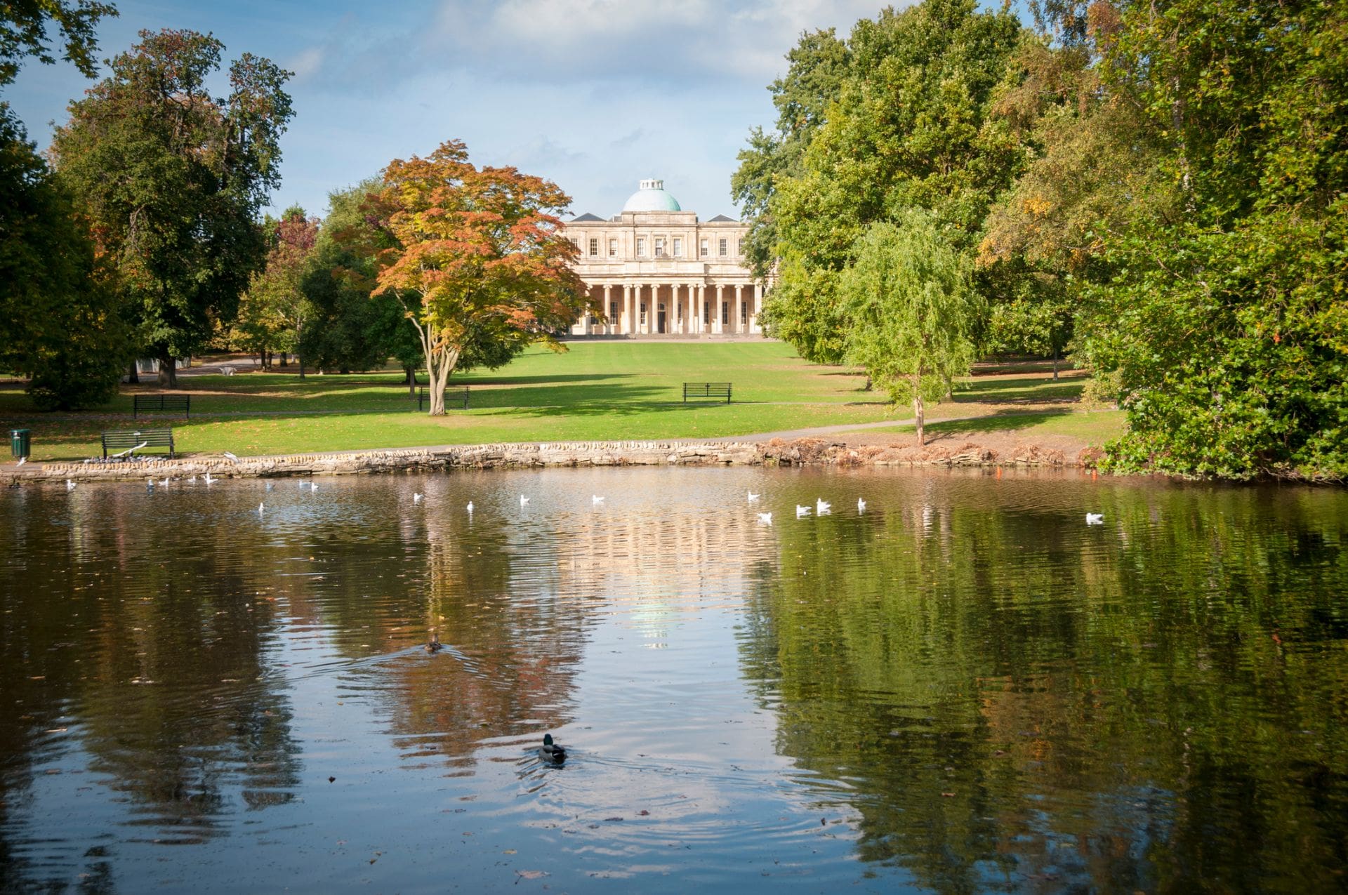 old-historic-building-overlooking-lake-in-autumn-at-pittville-park-in-cheltenham