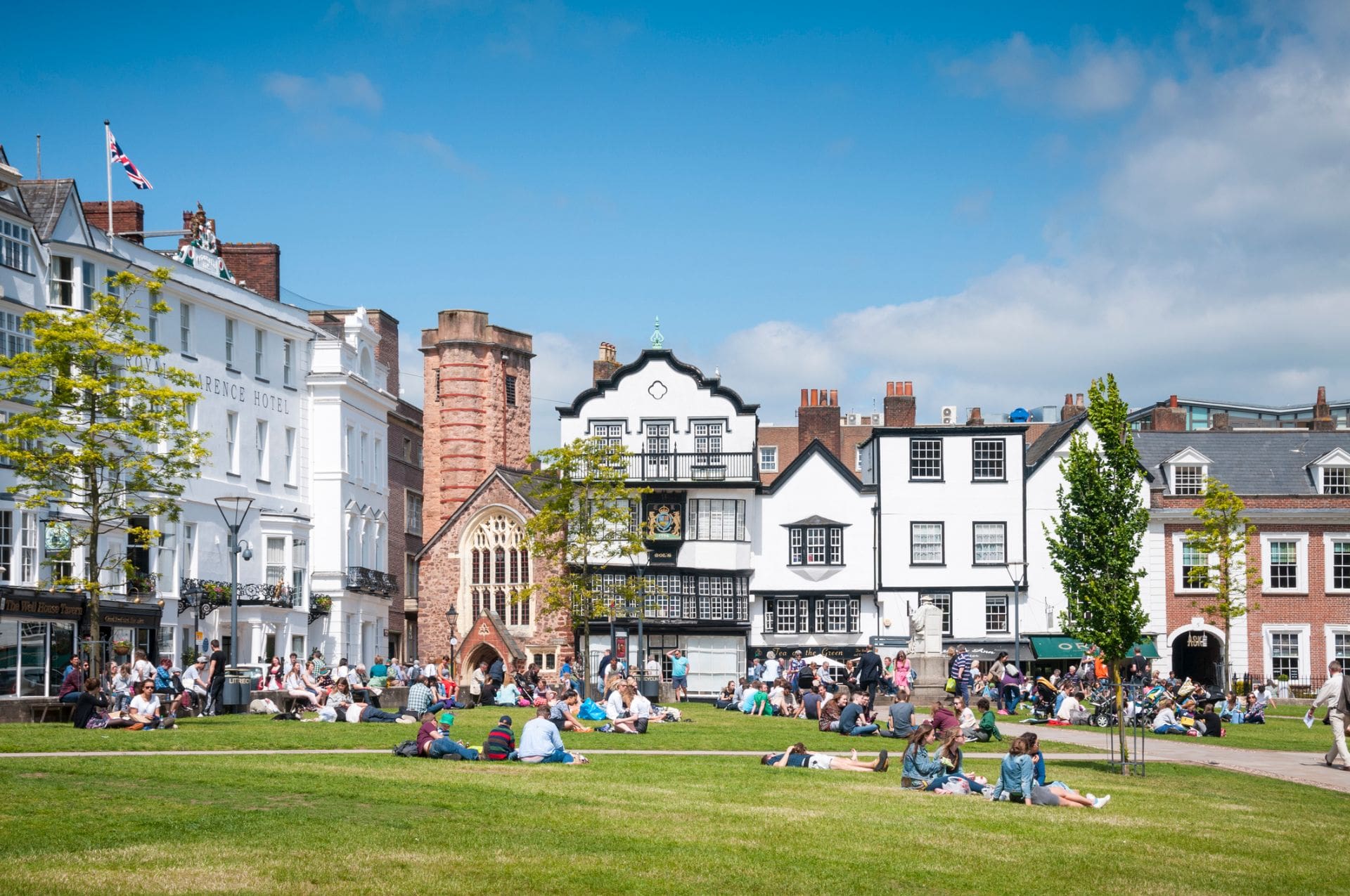 people-laying-on-grass-in-city-centre-in-front-of-cafes-shops-and-hotels-on-sunny-day-exeter-devon