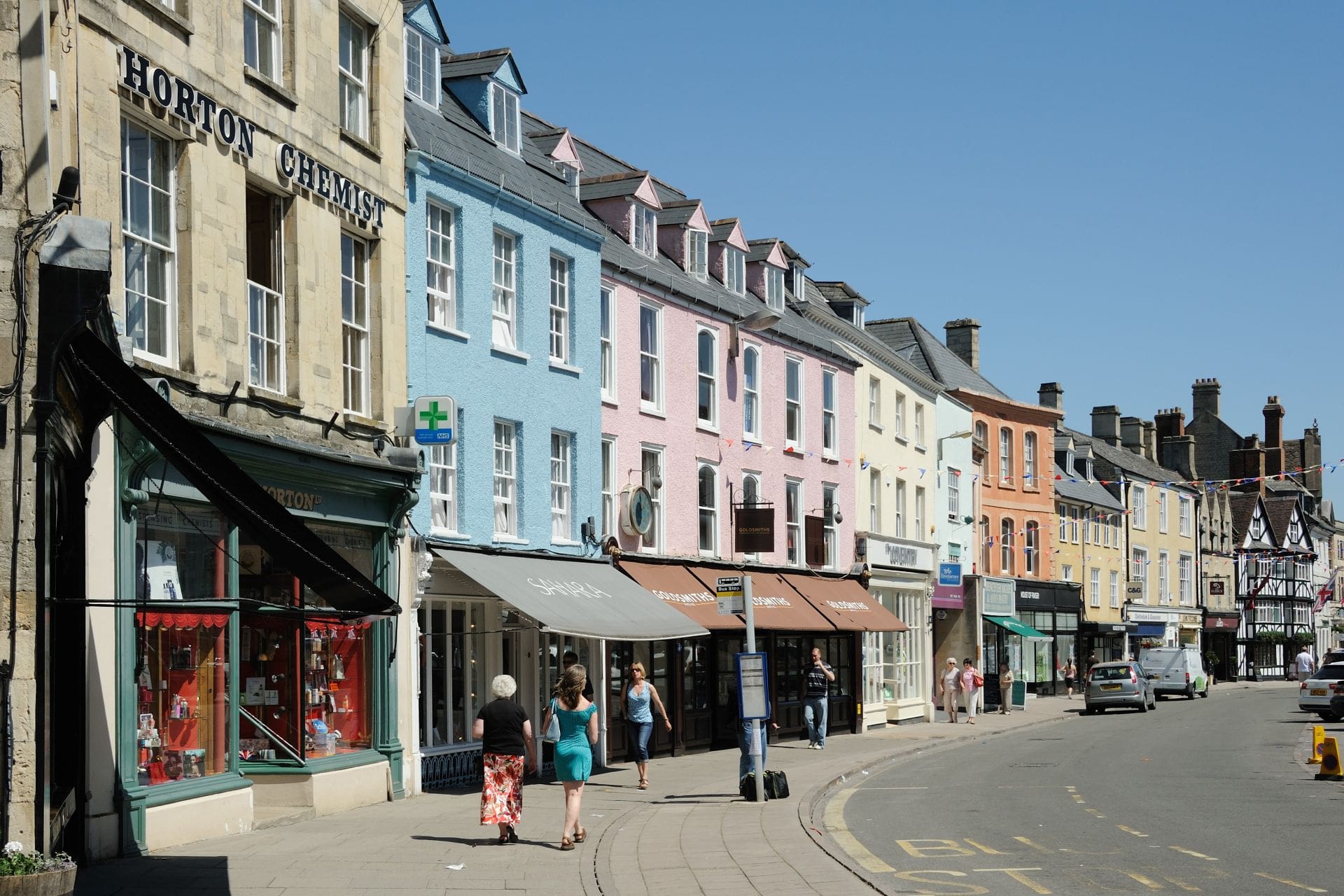 people-walking-down-british-high-street-with-colourful-shops-on-sunny-day-in-cirencester-gloucestershire