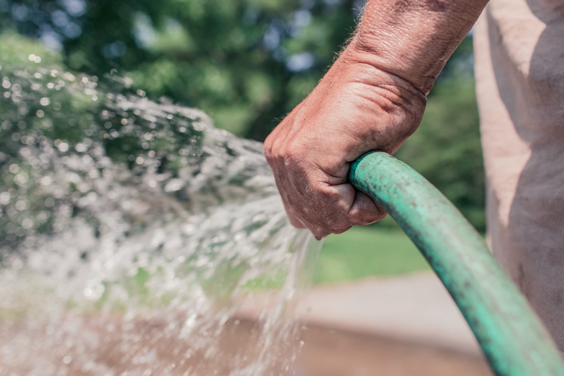 man's-hand-holding-green-hose-with-water-coming-out-of-it