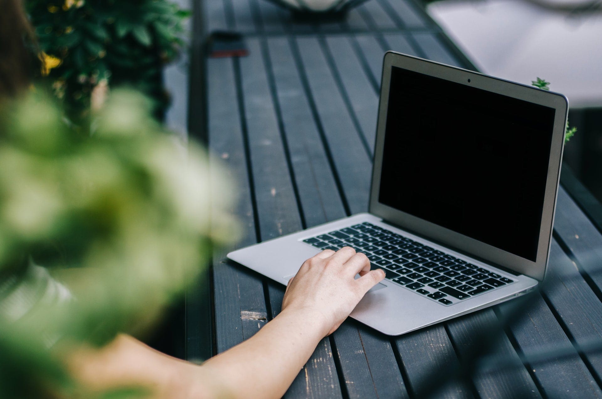 women-sat-on-bench-outside-using-laptop-on-table